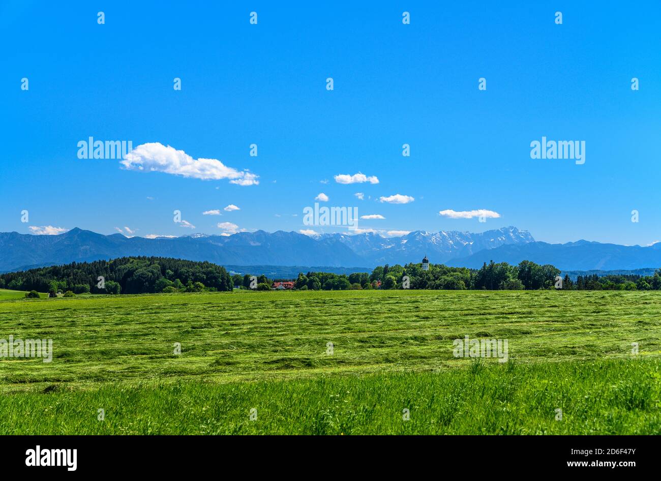 Germania, Baviera, alta Baviera, Tölzer Land, Münsing, distretto Holzhausen, paesaggio culturale e vista sulla città con la chiesa parrocchiale San Giovanni Battista contro le montagne Wetterstein con Zugspitze Foto Stock