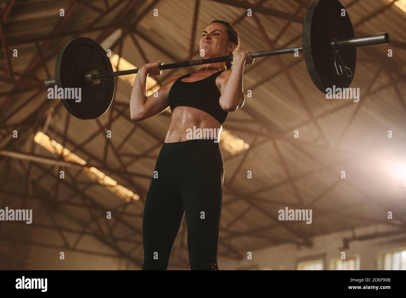 donna in forma fisica che si allena con un barbell pesante. Atleta forte che solleva pesi pesanti. Esecuzione di un allenamento strappato. Foto Stock