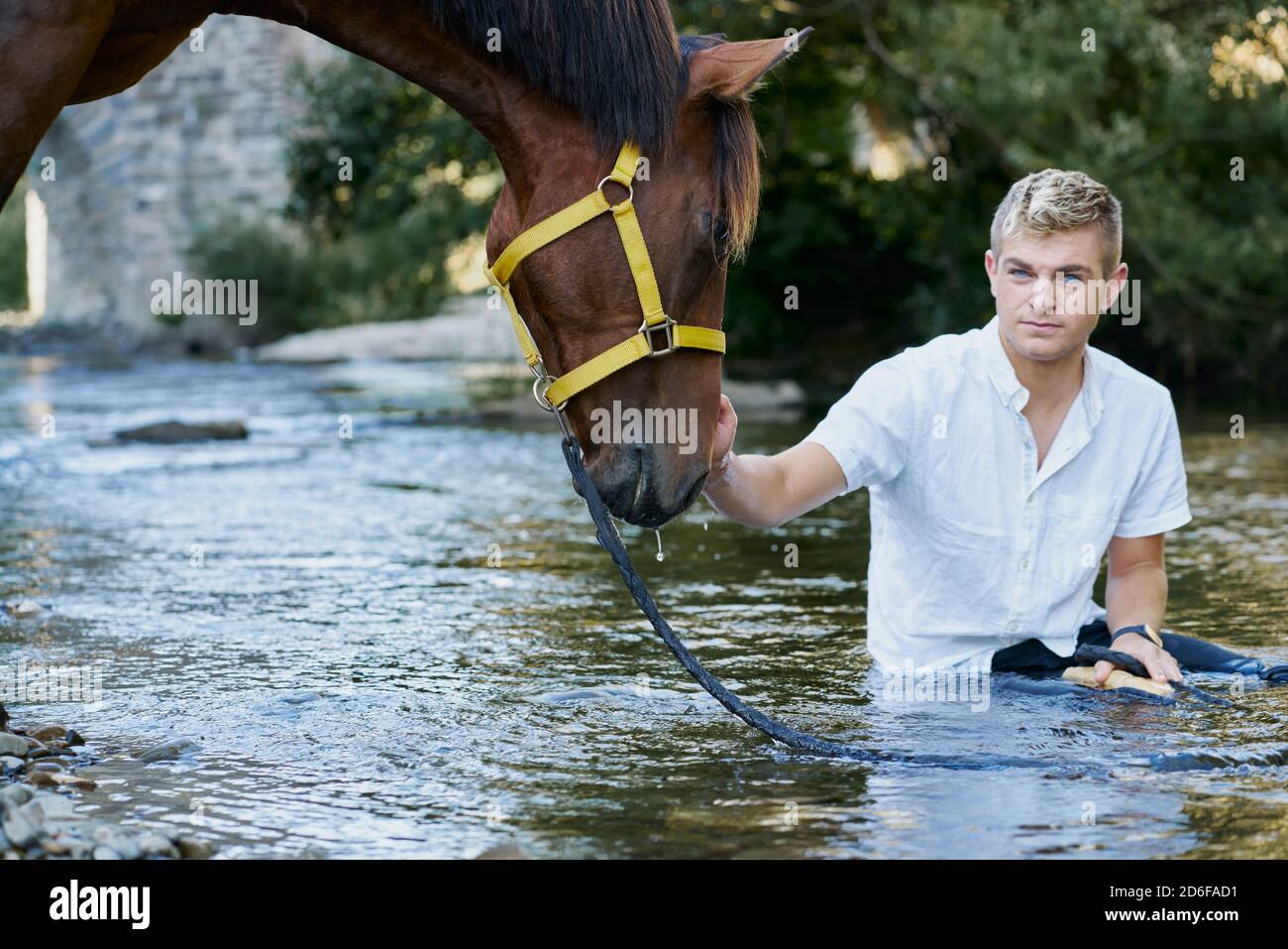 Ritratto di un giovane biondo con un cavallo un fiume Foto Stock