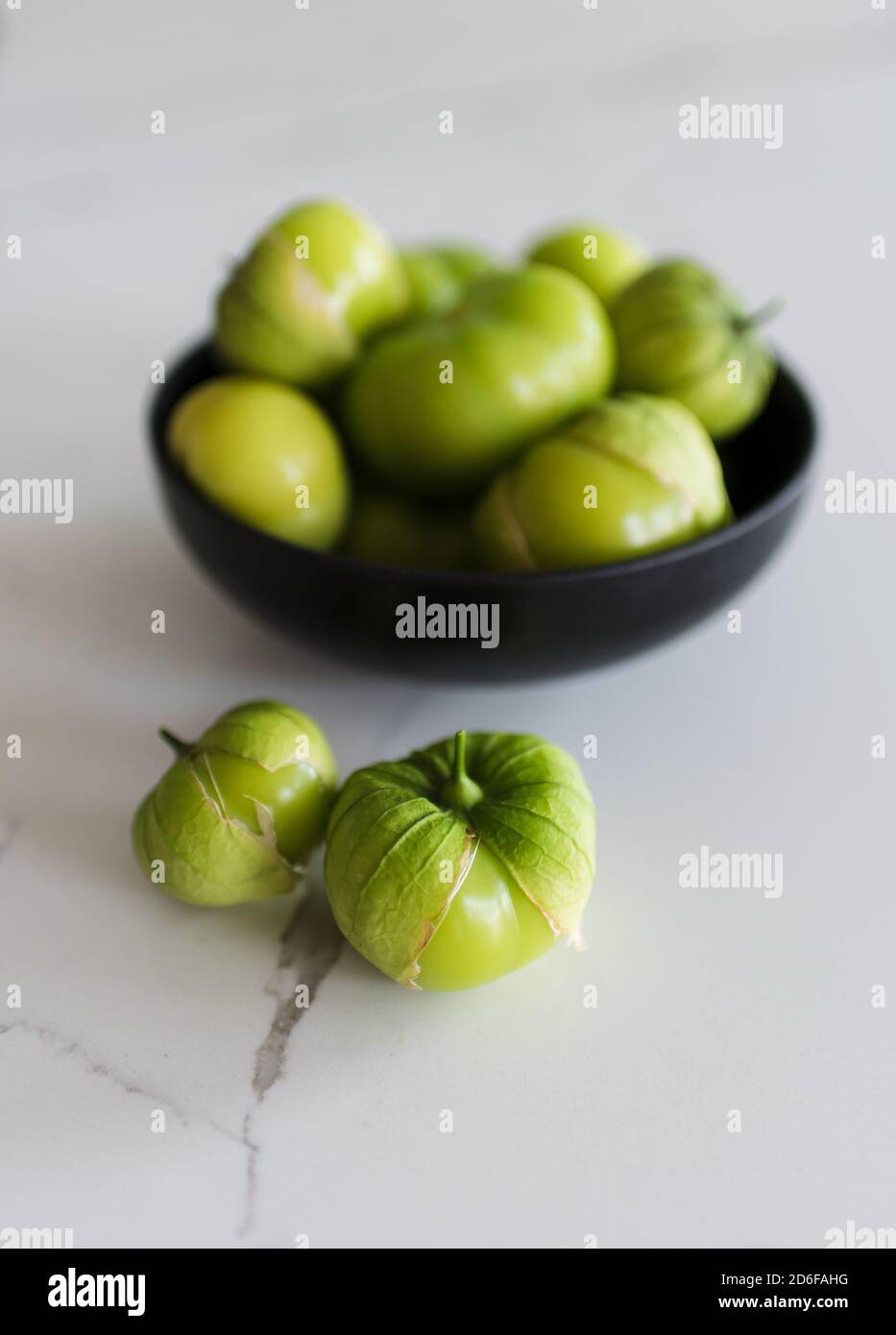 Ciotola di frutta fresca verde tomatillo su un bancone di quarzo bianco. Foto Stock