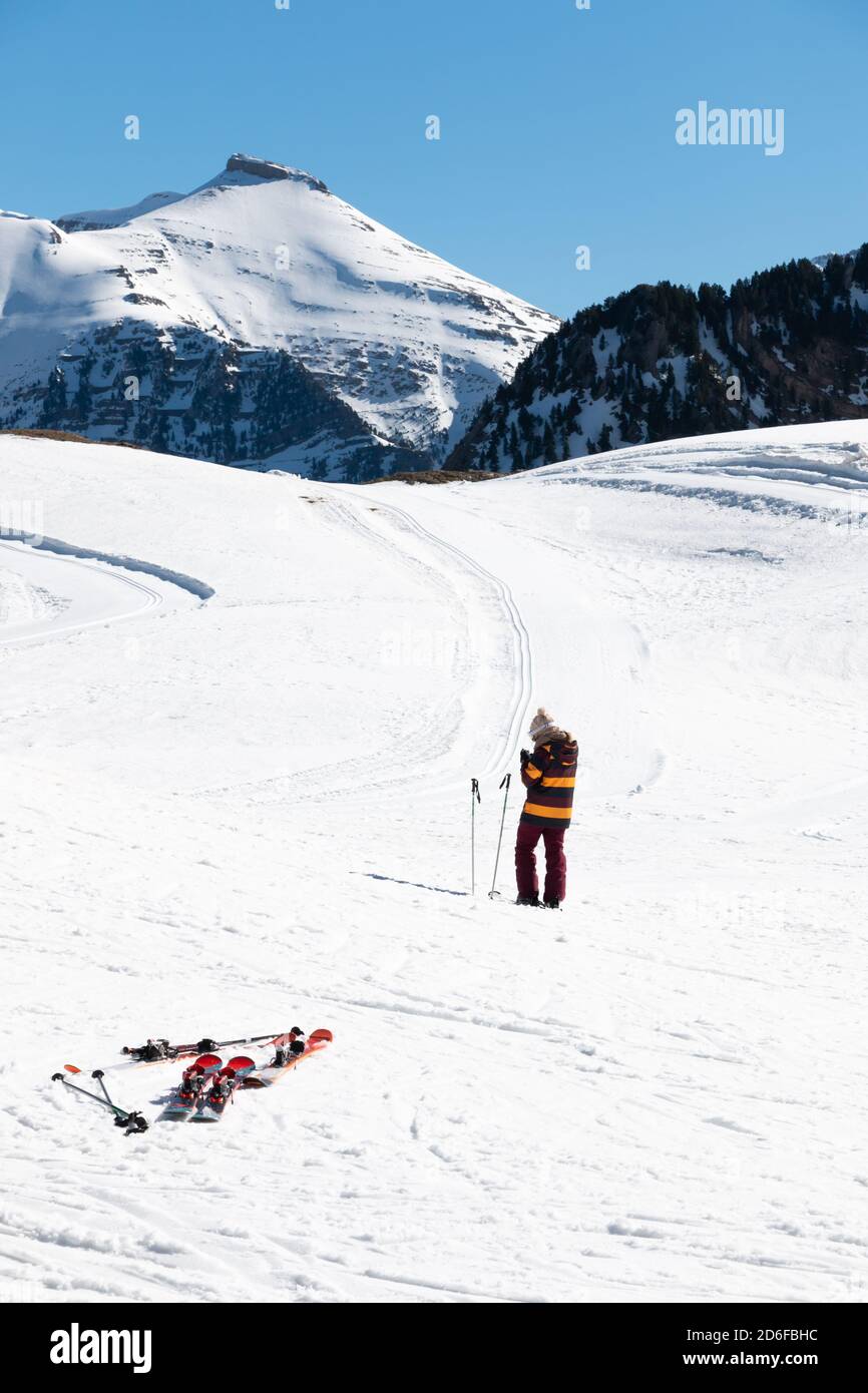 Una sciatrice femminile irriconoscibile consulta la sua mobilità nel mezzo di una pista da sci con alcuni sci in primo piano. Concetto di sci Foto Stock