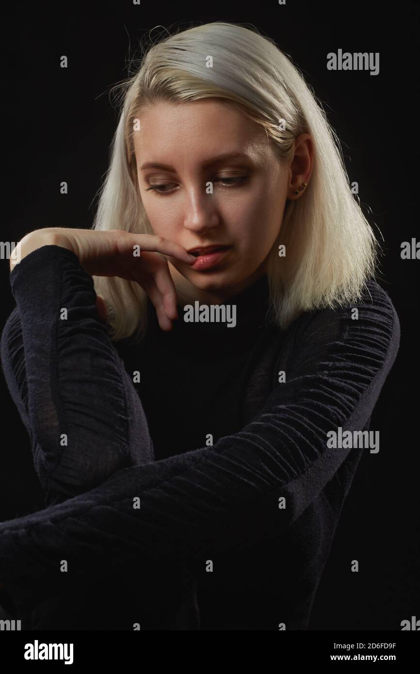 grave giovane donna stressata su sfondo nero guardando verso il basso Foto Stock