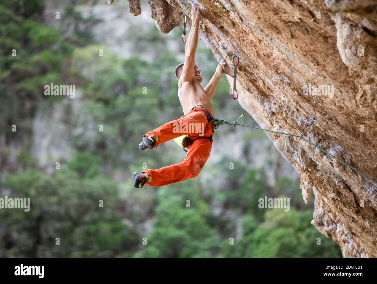 Giovane arrampicatore maschio dopo aver saltato e aggrappato piccole maniglie sulla scogliera a strapiombo Foto Stock
