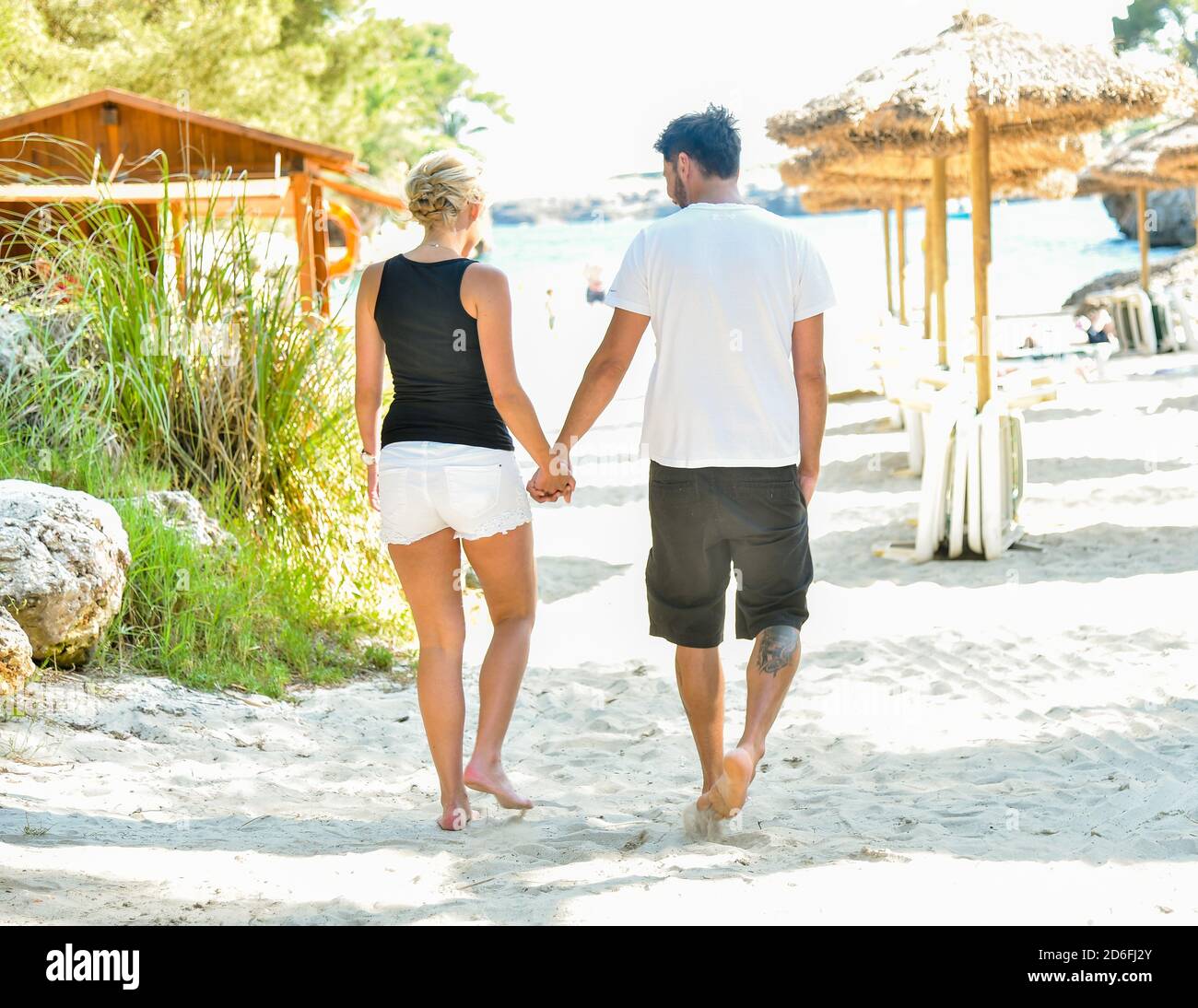 Uomini e donne che camminano romanticamente su un resort sulla spiaggia tenendo le mani Foto Stock