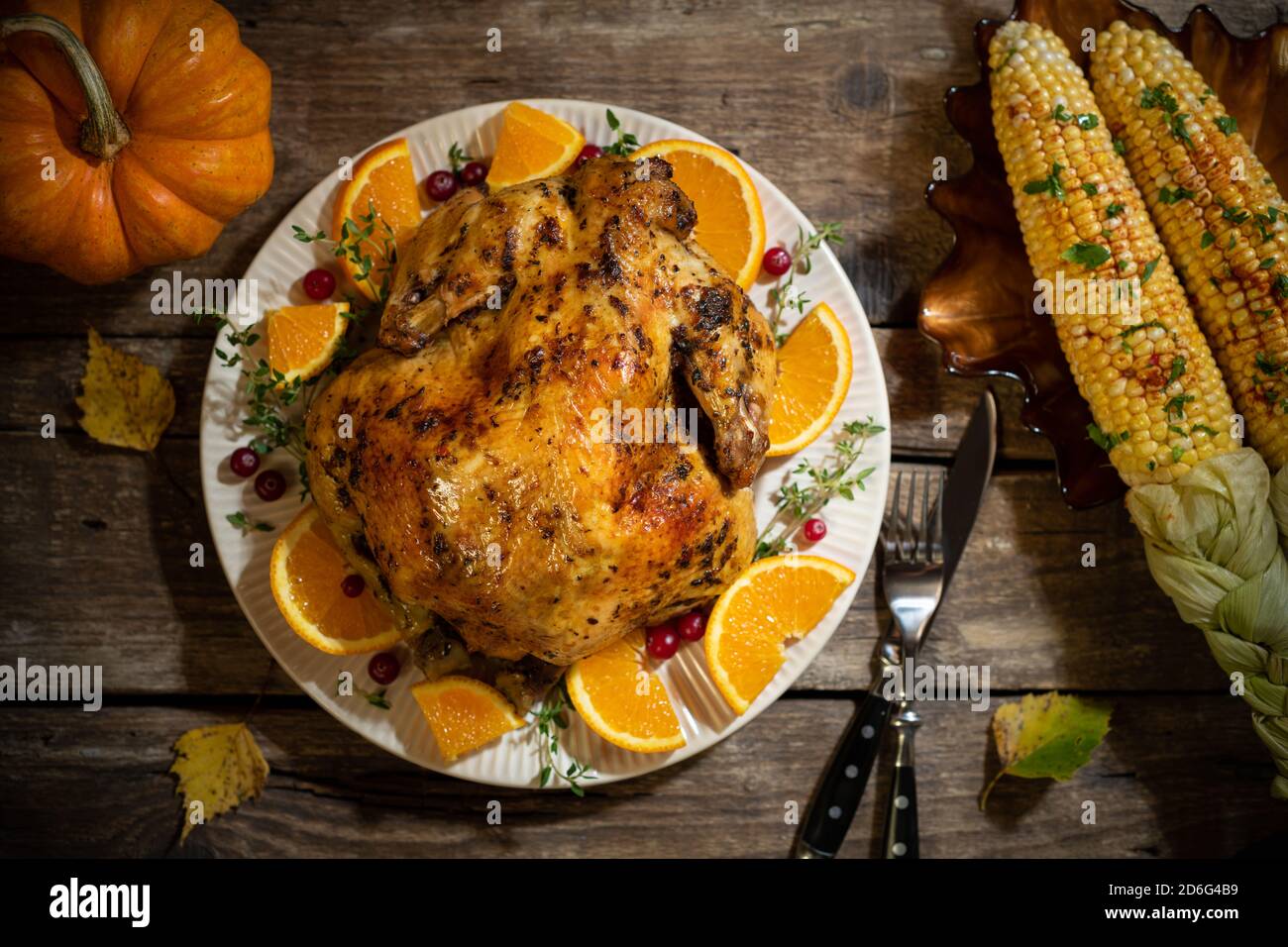 Composizioni autunnali di ringraziamento. Pollo arrosto o tacchino con agrumi e spezie, mais per celebrazioni giorno di ringraziamento su tavola di legno. ta festiva Foto Stock