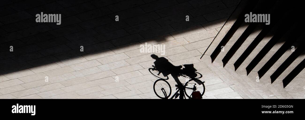 Profilo astratto dell'ombra di sfondo di una persona che sale su una bicicletta accanto alle scale all'aperto, seppia ad alto contrasto bianco e nero Foto Stock