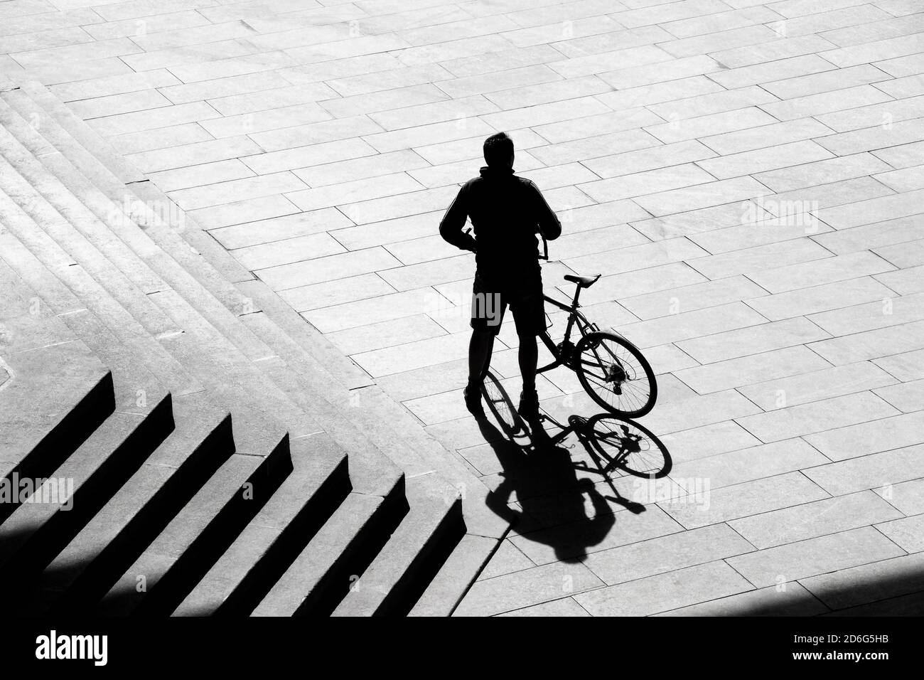 Belgrado, Serbia - 09 ottobre 2020: Sagoma d'ombra di una persona in piedi accanto a una bicicletta accanto alle scale esterne della città, da dietro in vista ad alto angolo Foto Stock