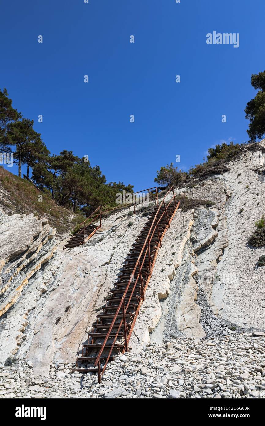 Una vecchia scala in metallo e massicce rocce bianche su una spiaggia selvaggia. Il sentiero per il campeggio attraversa la foresta. Paesaggio estivo in una giornata limpida Foto Stock