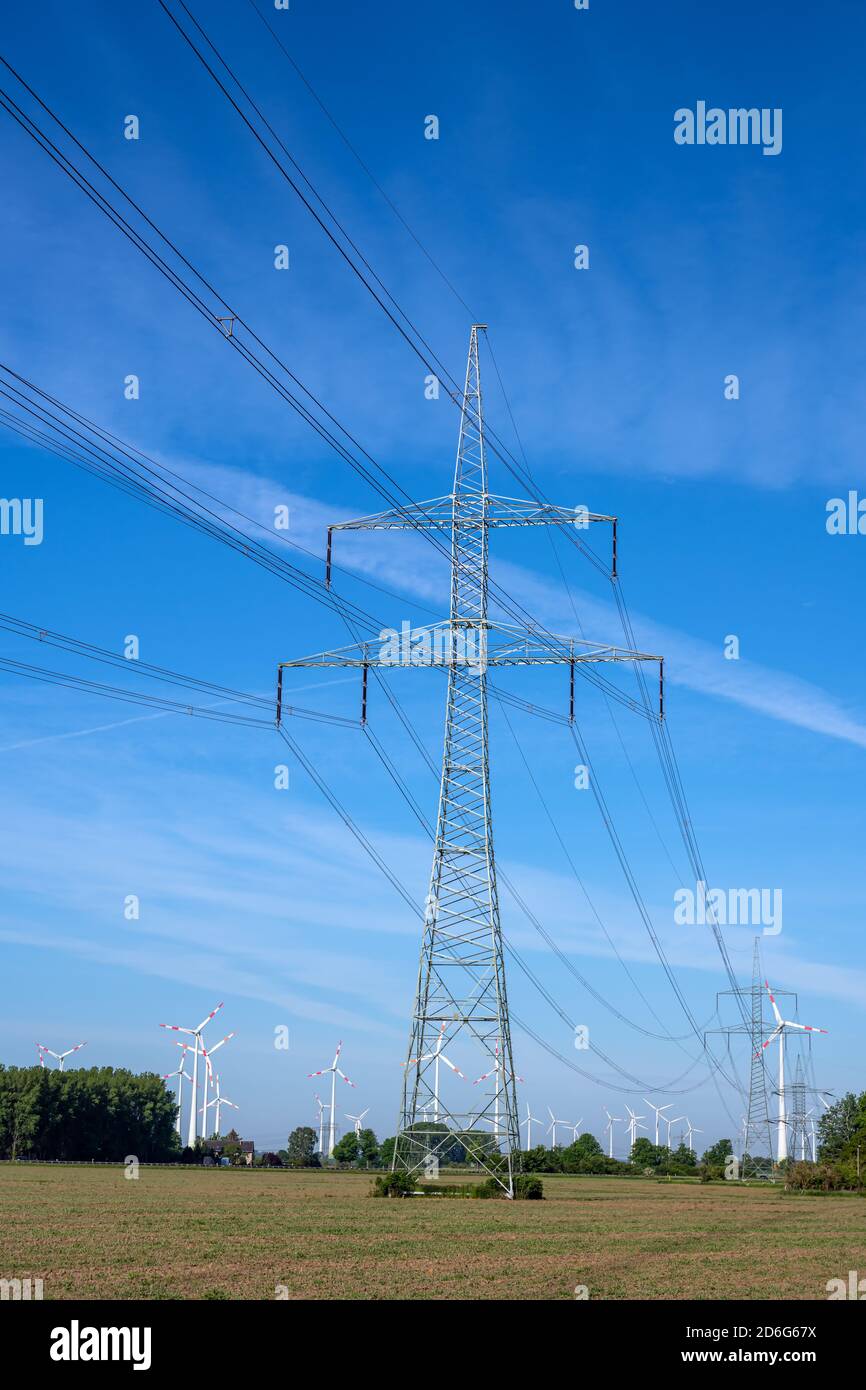 Pilone elettrico e linee elettriche con turbine eoliche nel indietro Foto Stock