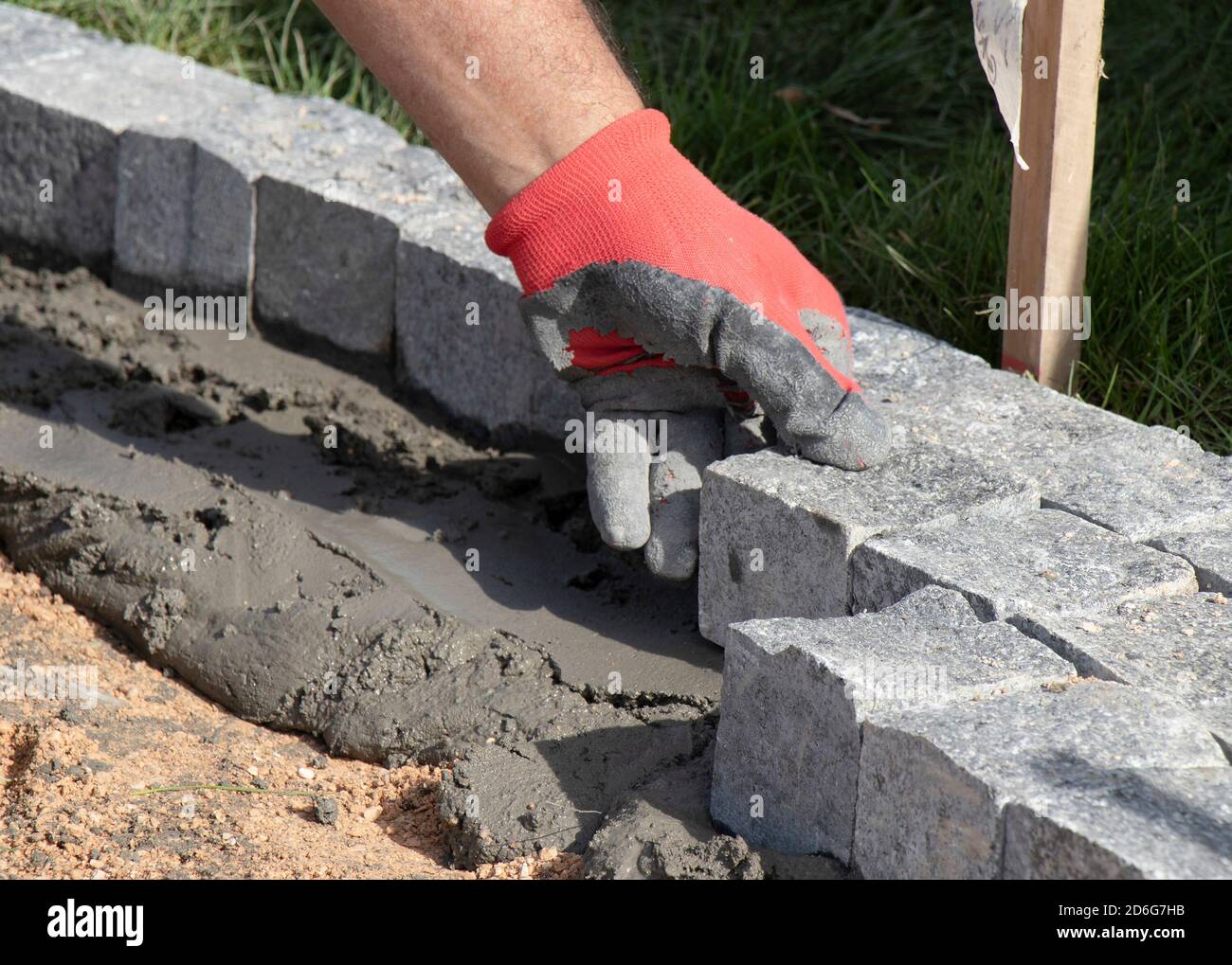 Mani in guanti di un lavoratore costruttore che posa sul granito ciottolato sett su sabbia e Malta, marciapiede pavimentazione Foto Stock