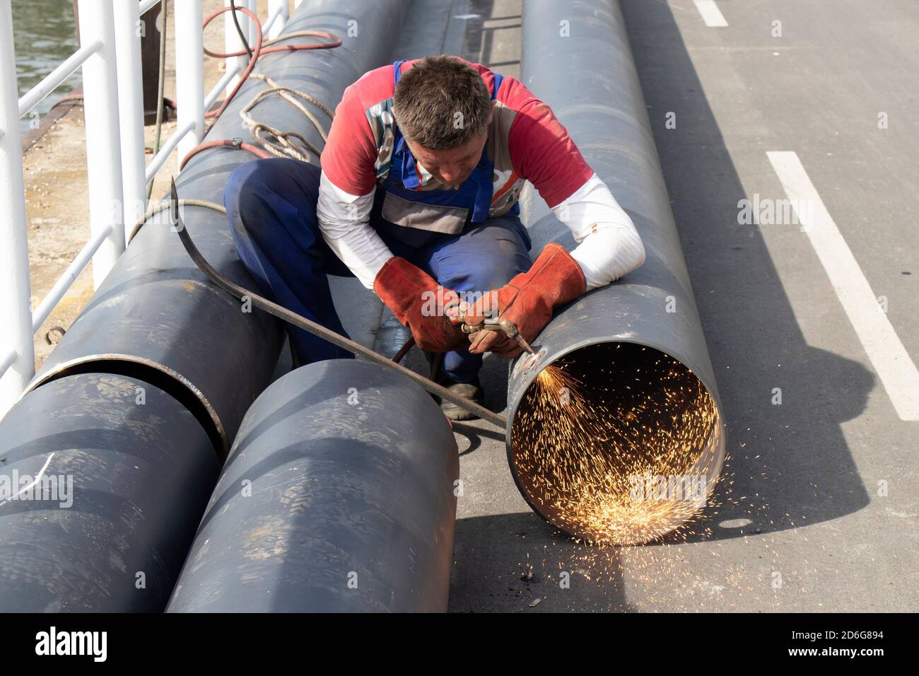 Belgrado, Serbia - 09 ottobre 2020: Saldatore che taglia un ampio tubo metallico con una torcia da taglio ad ossi-combustibile, con fiamma e scintille, all'aperto sulla riva del fiume Foto Stock