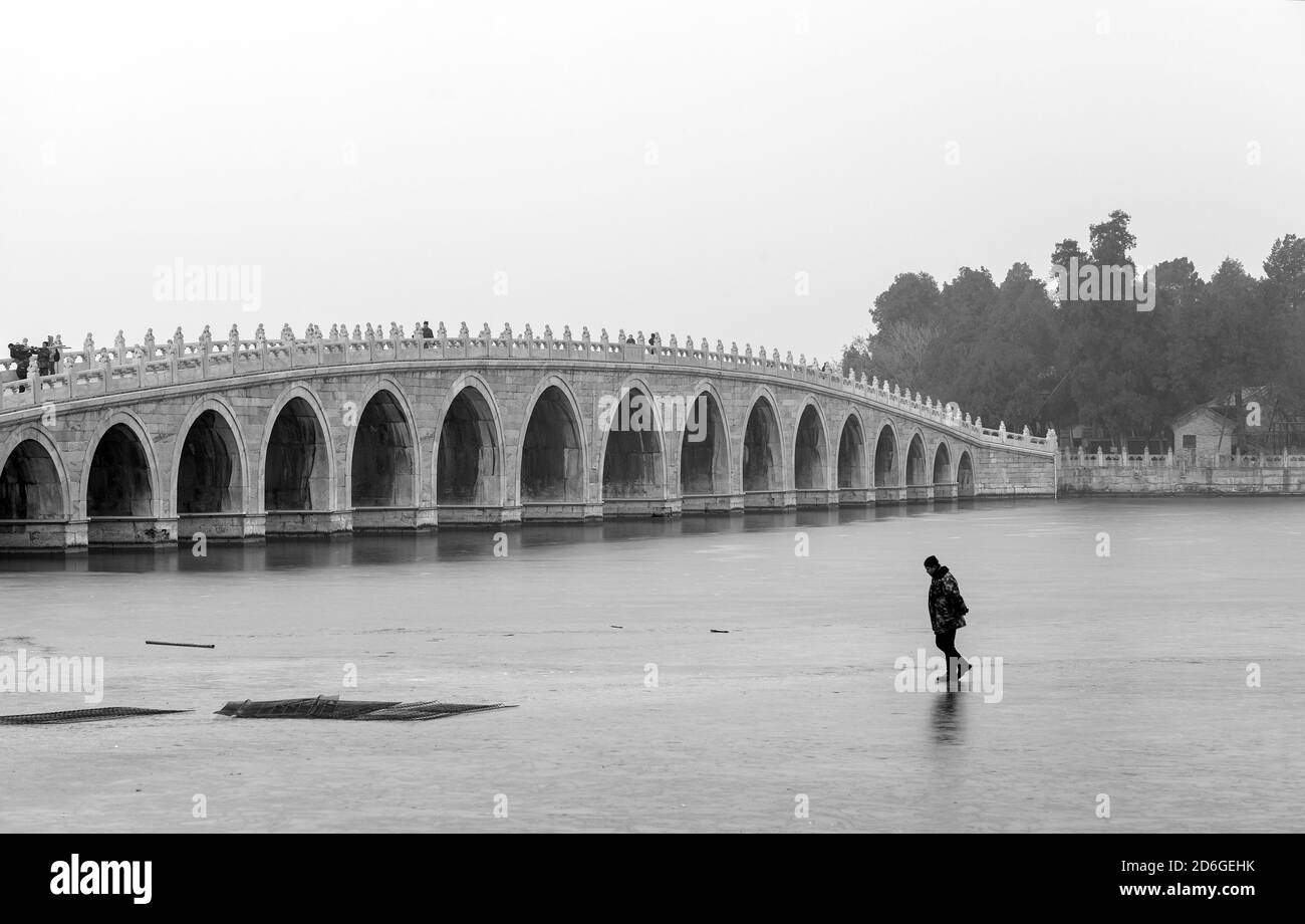 Un uomo che cammina sul ghiaccio, vicino al Ponte dell'Arco di Seventeen (Shiqikong Qiao) nel Lago di Kunming, Pechino, Cina. Una giornata invernale in nebbia Foto Stock
