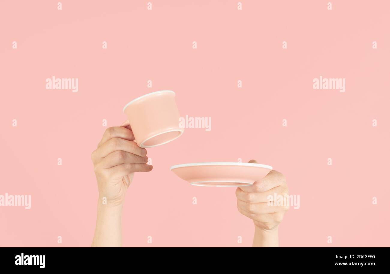 Mani che tengono su una tazza e un piatto su uno sfondo rosa morbido, con la copia spazio Foto Stock