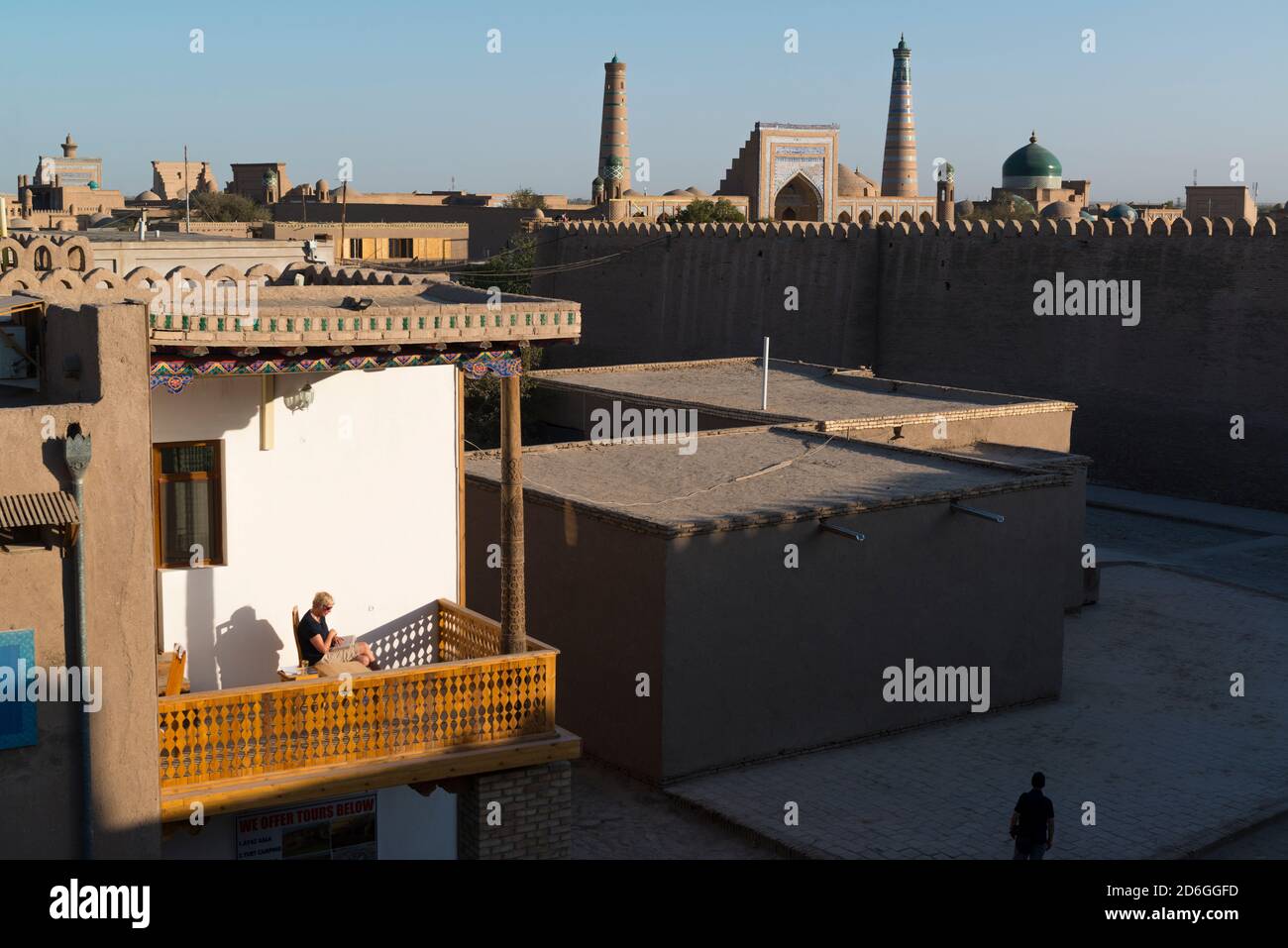 Donna turista occidentale leggere un libro su un balcone illuminato dal sole vicino a Itchan Kala, la città murata interna di Khiva, Uzbekistan. Foto Stock