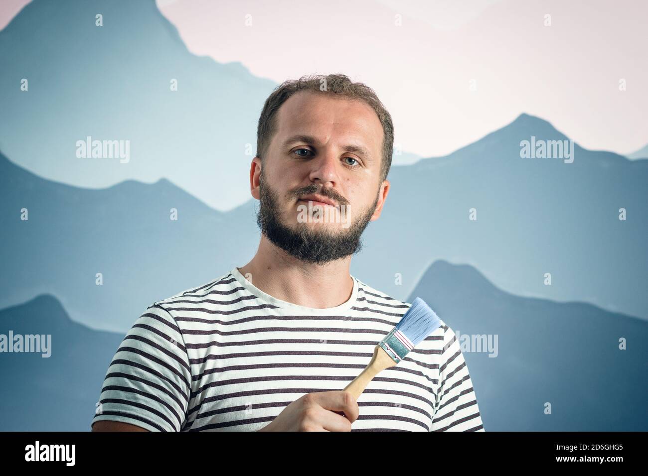 Uomo bearded pittore tenendo pennello davanti alla parete. Come fare le riparazioni voi stessi Foto Stock