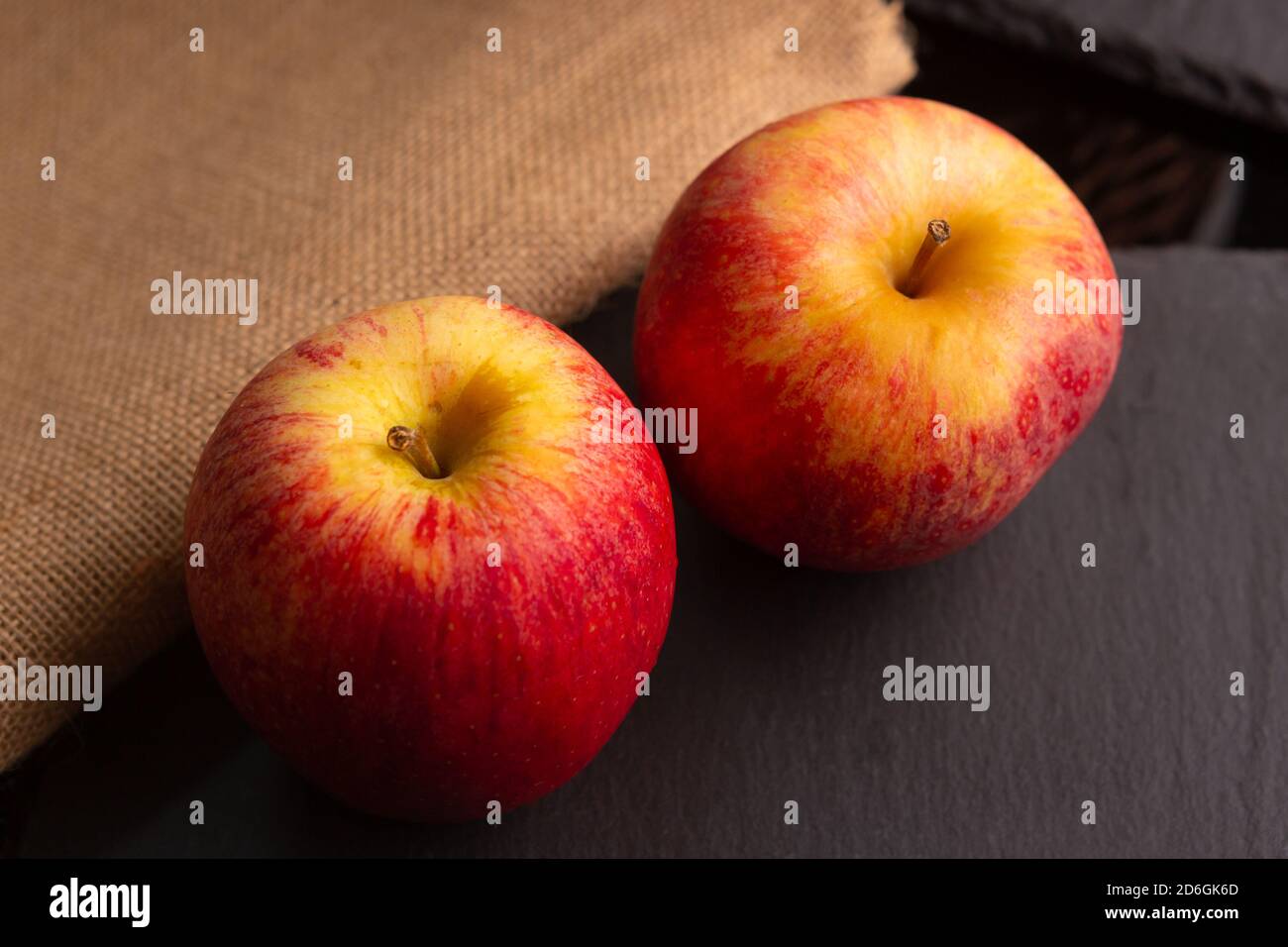 due mele rosse poste su un pezzo di ardesia dentro un ambiente poco luminoso Foto Stock