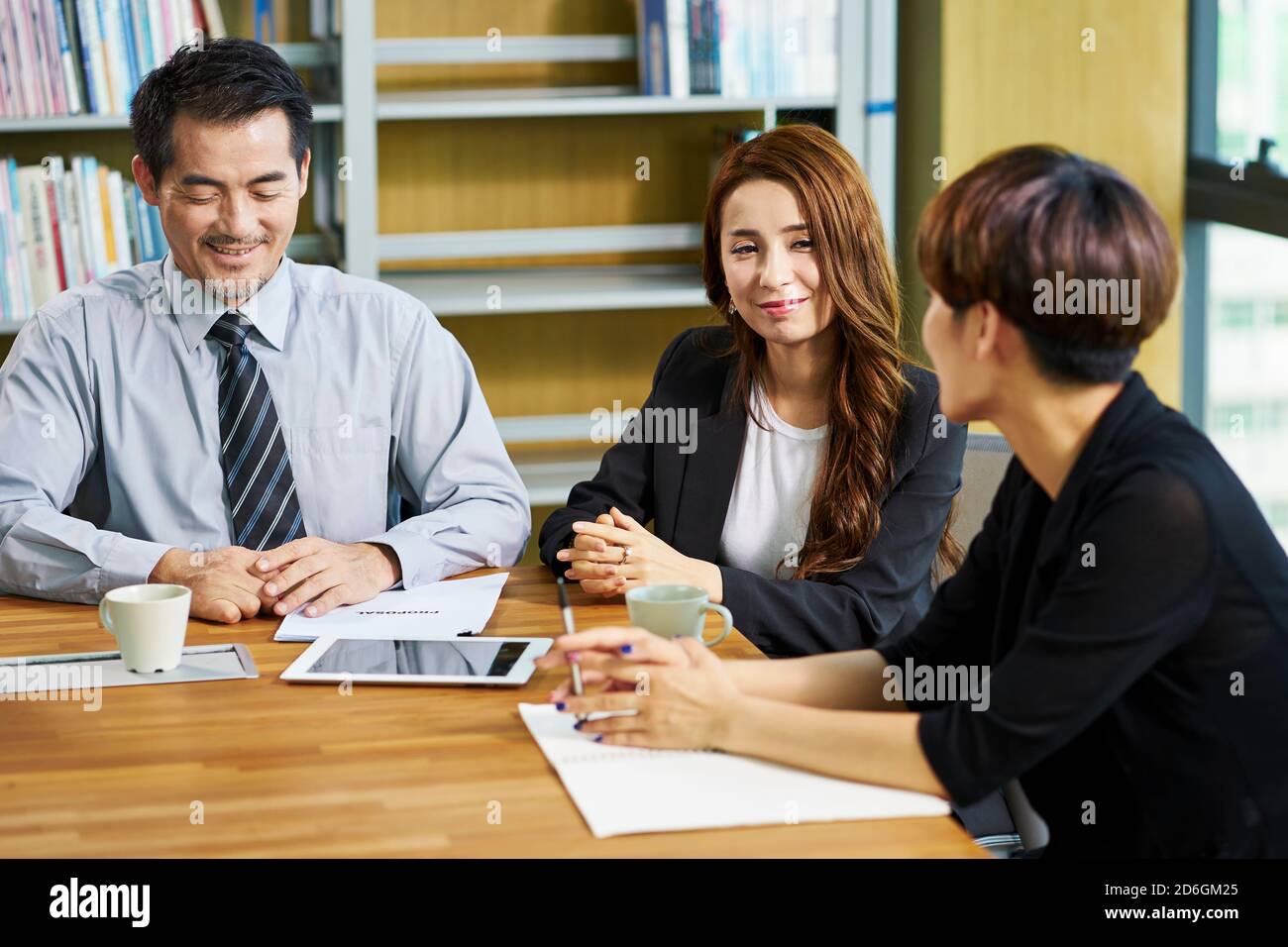 tre uomini e donne d'affari asiatici seduti alla scrivania in discussione proposta commerciale in ufficio Foto Stock