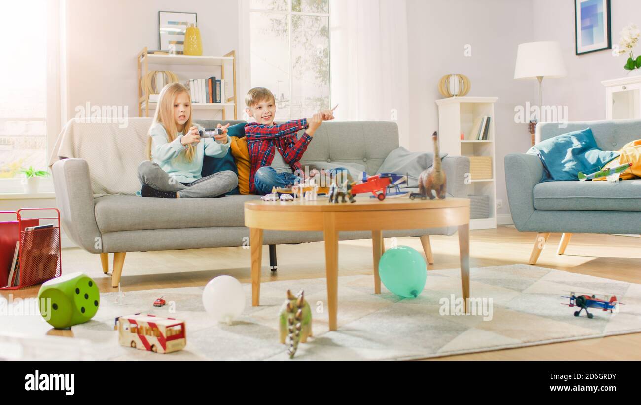 A casa: Ragazza carina giocando nella console di videogiochi, utilizzando il joystick Controller, il suo Brother Cheers più giovane per lei. Bambini felici che giocano ai videogiochi. Foto Stock