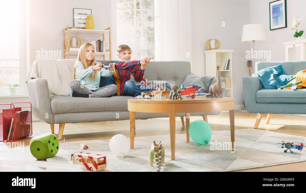 A casa: Ragazza carina giocando nella console di videogiochi, utilizzando il joystick Controller, il suo Brother Cheers più giovane per lei. Bambini felici che giocano ai videogiochi. Foto Stock