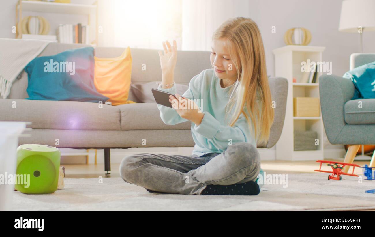Smart cute Girl seduto su un tappeto giocando in Video Game sul suo smartphone, tiene e utilizza il cellulare in modalità orizzontale. Il bambino ha divertimento Foto Stock