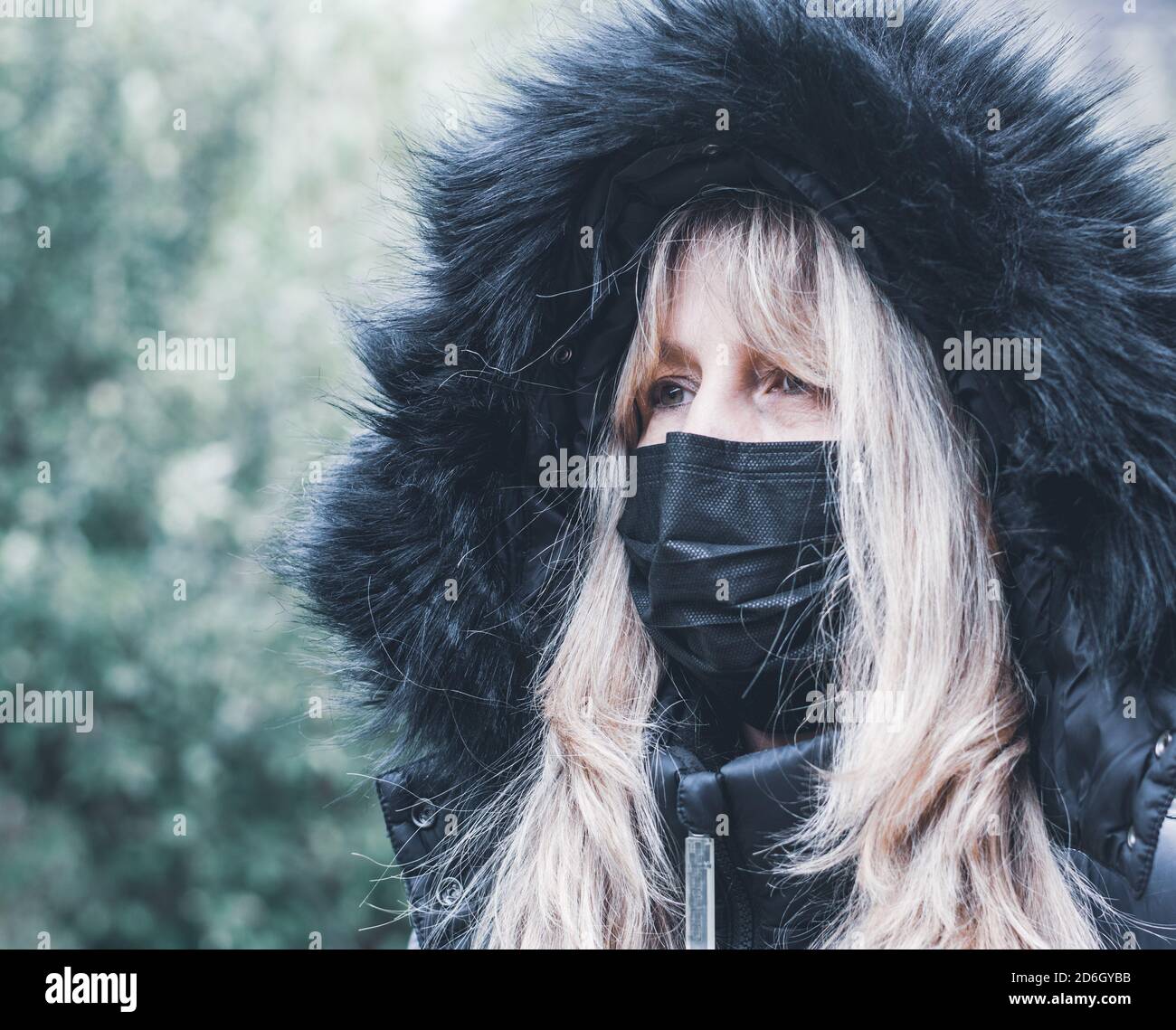 ritratto di una donna in un cappotto invernale con pelliccia cappuccio e maschera facciale per la protezione da virus Foto Stock
