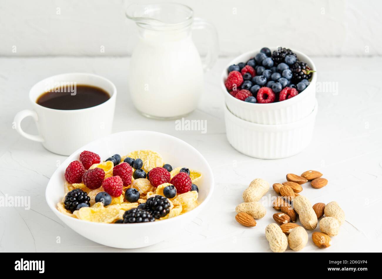 Colazione sana con cornflakes, lamponi, more, mirtilli, arachidi, latte e caffè su sfondo bianco. Spazio di copia, piatto, healt Foto Stock
