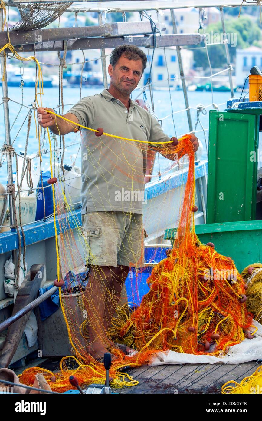 Un pescatore a bordo di una barca da pesca controlla le sue reti per i buchi nel porto dell'isola greca di Kastellorizo, altrimenti conosciuta come isola di Meis. Foto Stock