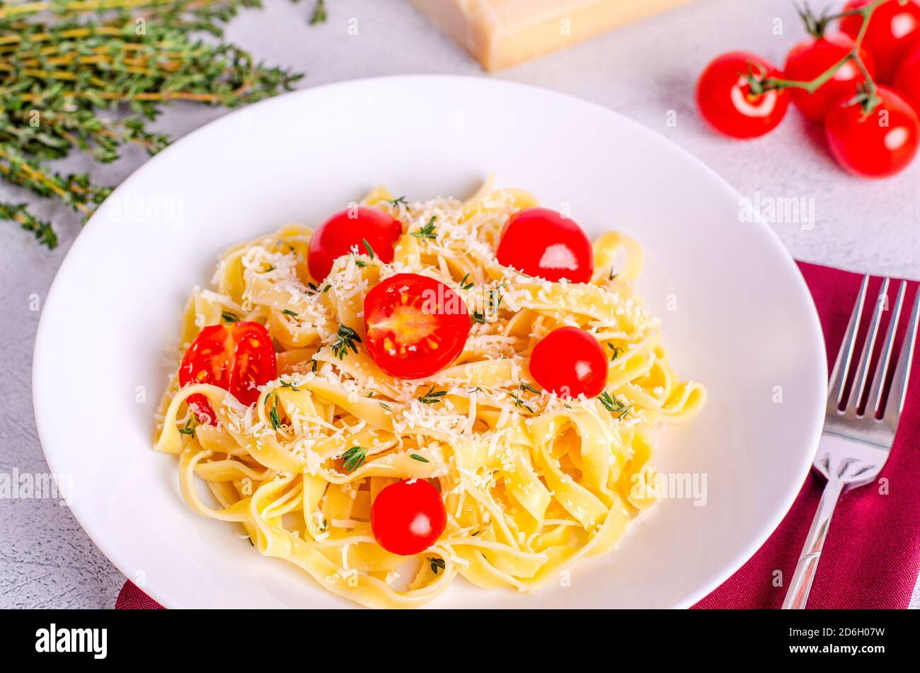 Pasta di fettuccine fatta in casa con pomodori, timo, parmigiano in un piatto bianco con un tovagliolo rosso su uno sfondo chiaro. Piatto tradizionale italiano. Co Foto Stock