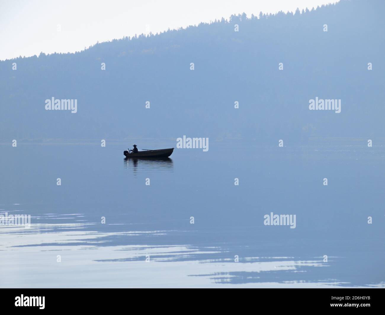 pescatore in barca silhouette sul lago calmo con montagna riflettente su acqua Foto Stock