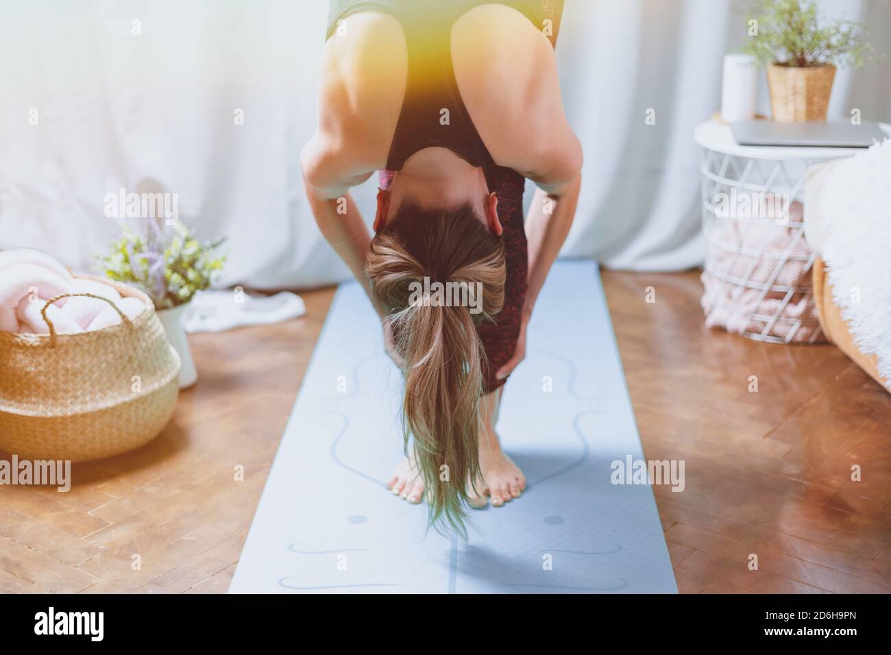 Primo piano giovane donna sportiva attraente che pratica yoga, in piedi avanti piega esercizio, testa a ginocchia, uttanasana posa, allenarsi a casa in vita Foto Stock