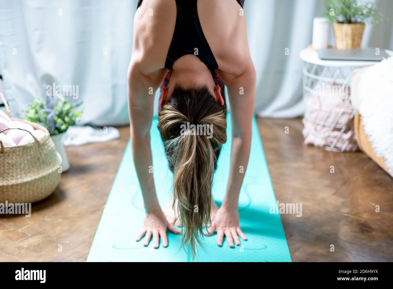Giovane attraente donna sportiva che pratica yoga, in piedi avanti piega esercizio, testa a ginocchia, uttanasana posa, allenarsi a casa in soggiorno. SpO Foto Stock