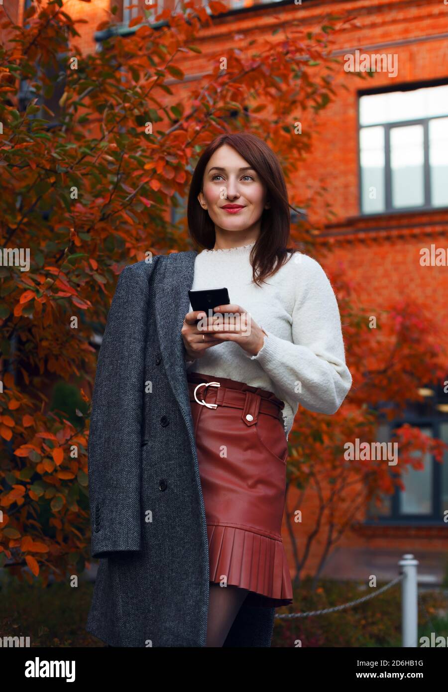 Bella donna che controlla le sue reti sociali mentre attende qualcuno per datare. Donna sorridente che tiene lo smartphone. Foto Stock