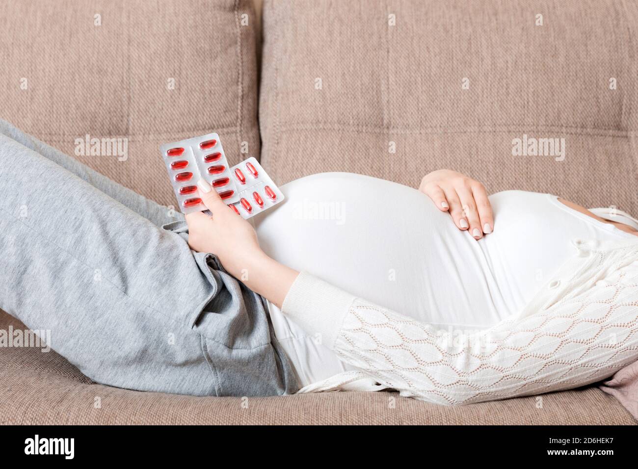 Sezione centrale della donna incinta che prende la pillola di vitamina sul divano a casa. Foto Stock