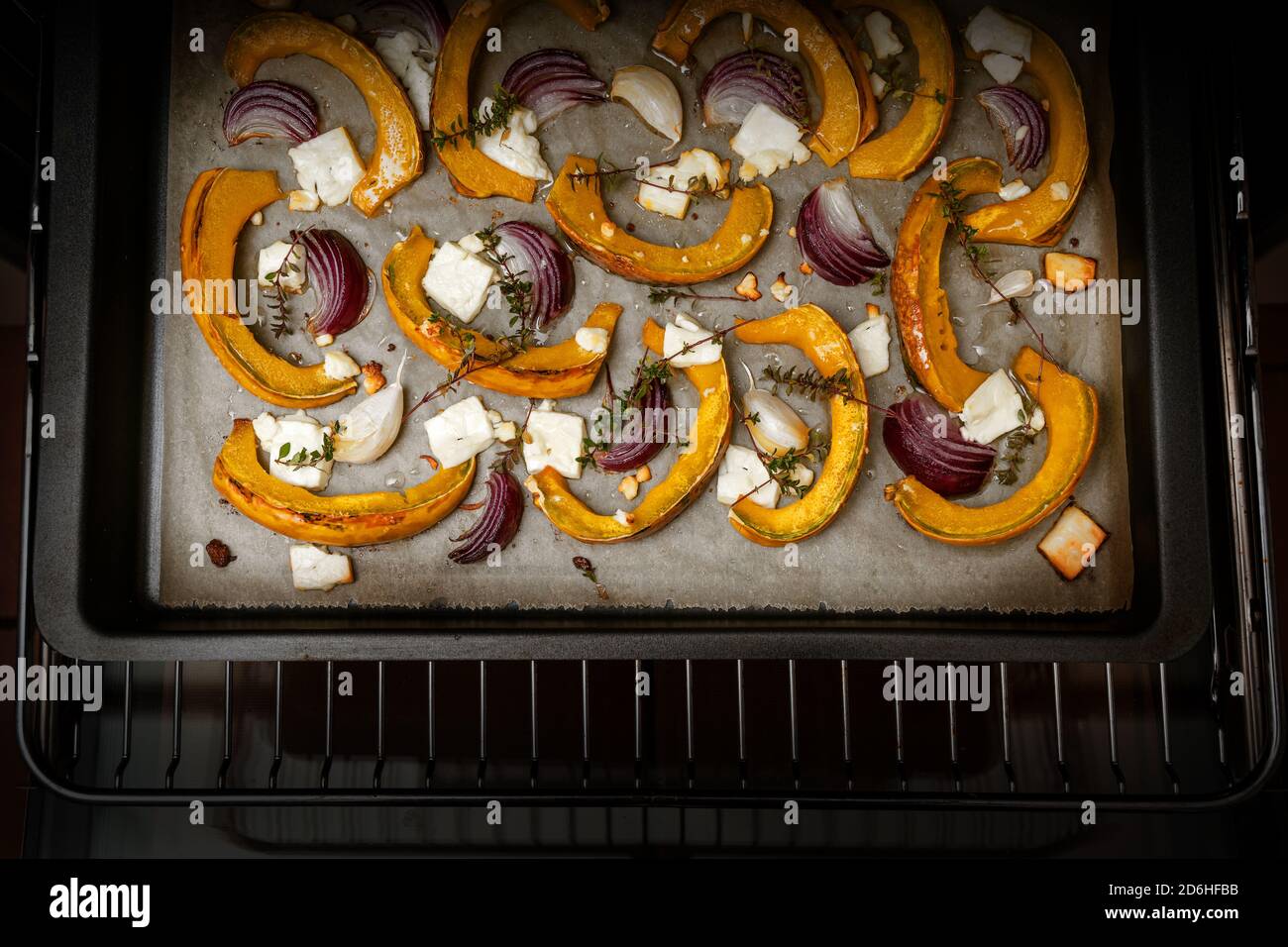 Fette di zucca o di zucca con cipolle rosse, aglio, formaggio feta e timo su una teglia in forno, pasto di verdure autunnali per il Ringraziamento e l'Hallo Foto Stock