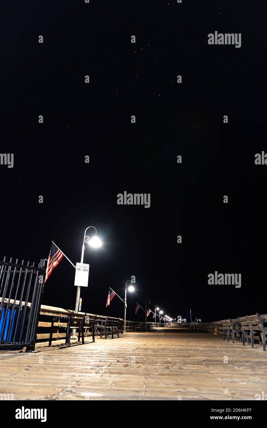 Le luci del molo illuminano la passerella in legno del molo di Ventura sotto Orion e altre costellazioni stellari nel cielo notturno. Foto Stock