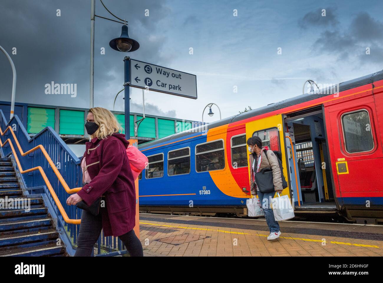 Due passeggeri di sesso femminile che indossano maschere facciali si staccano da un treno per pendolari presso una stazione locale. Foto Stock