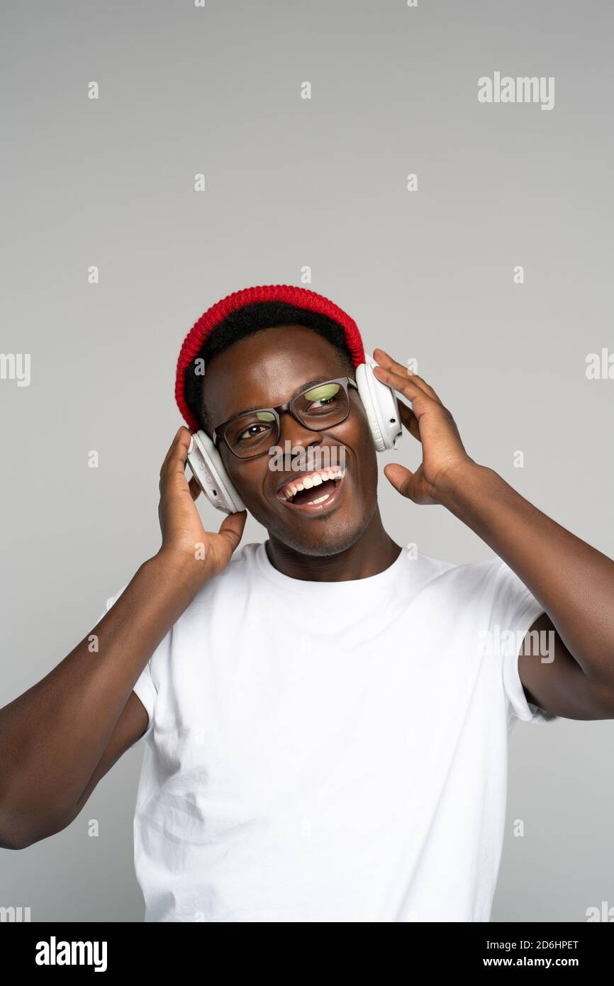 L'uomo afro-americano indossa cappelli rossi e occhiali, godendosi l'ascolto del nuovo album dell'artista, danze, fa movimenti alla musica, tocca hea wireless Foto Stock