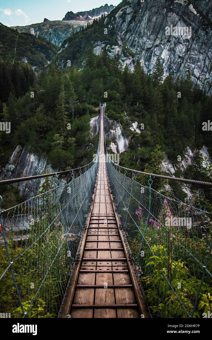 Ponte di legno lungo sopra la gola profonda con una spiaggia di fiume in fondo, tra le rocce. Montagne selvagge nelle Alpi svizzere Foto Stock