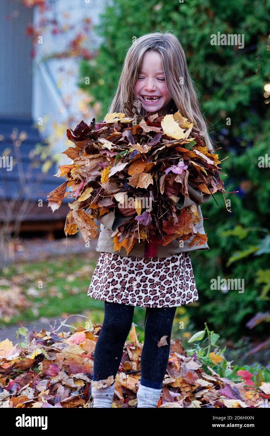 Una ragazza sorridente di 6 anni che tiene un pacchetto di foglie d'autunno Foto Stock