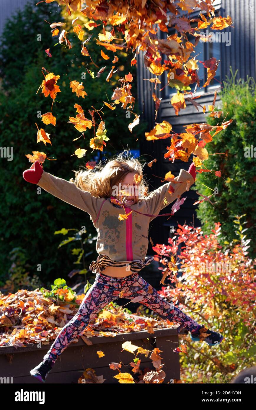 Una ragazza di 6 anni, saltando e lanciando giocando con foglie d'autunno Foto Stock