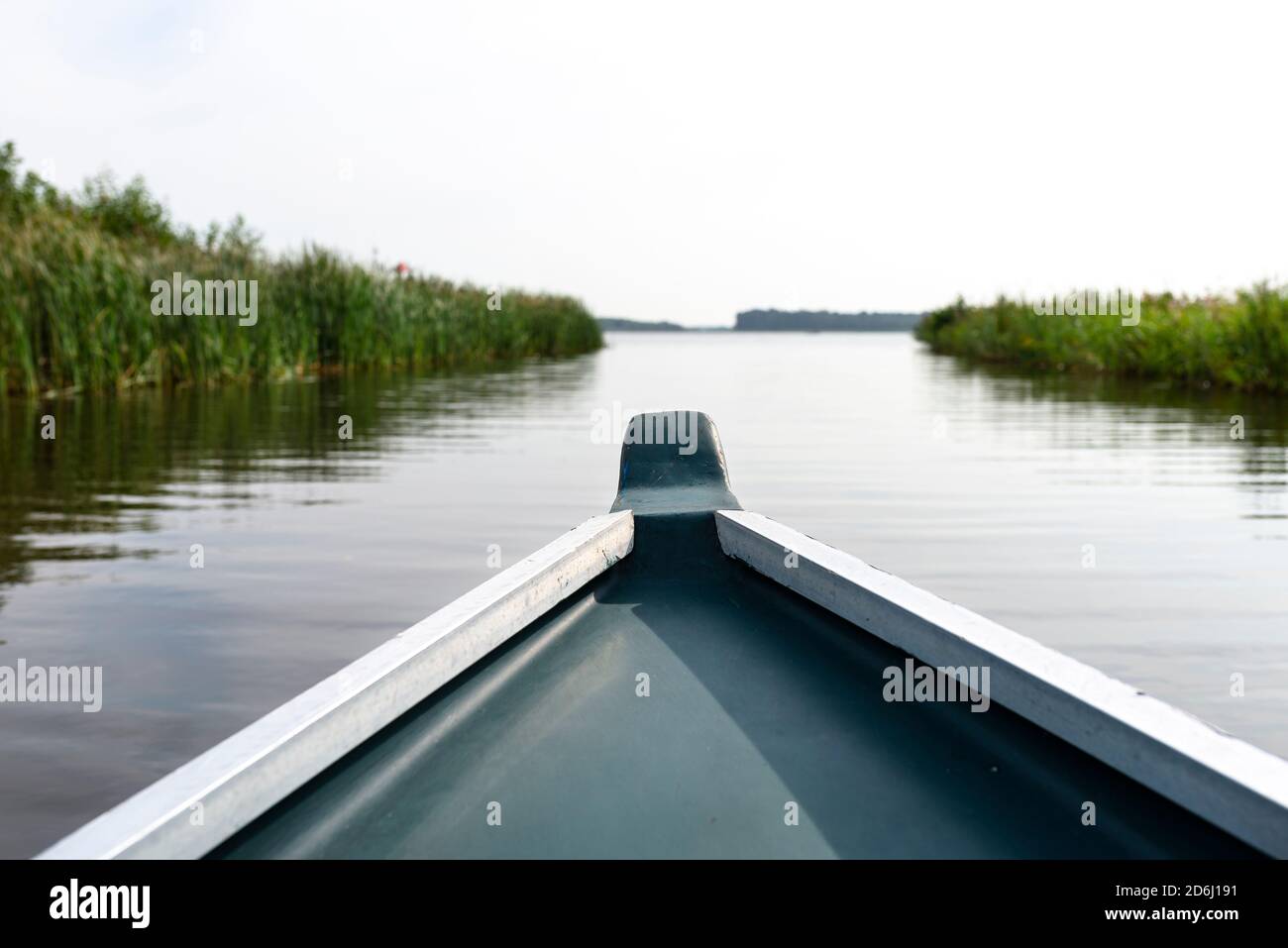 Foto scattata da una barca di legno, il prow della barca visibile, sullo sfondo un lago sfocato e canne. Foto Stock