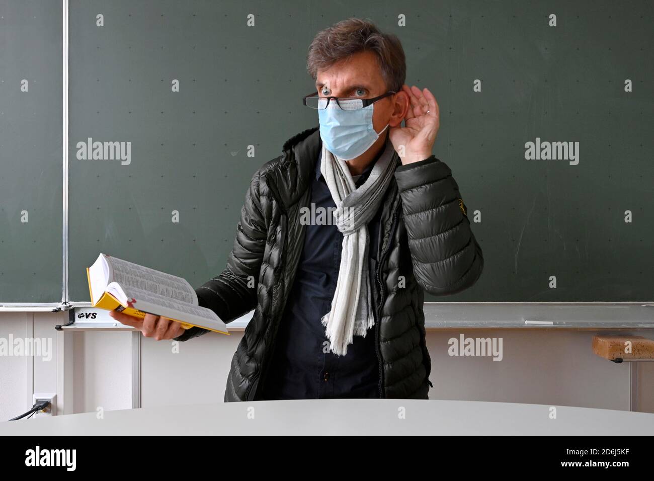 Insegnante con una spessa giacca invernale, sciarpa e maschera facciale in classe, mano sull'orecchio, problemi di comunicazione, crisi corona, Stoccarda, Baden-Wuerttemberg Foto Stock