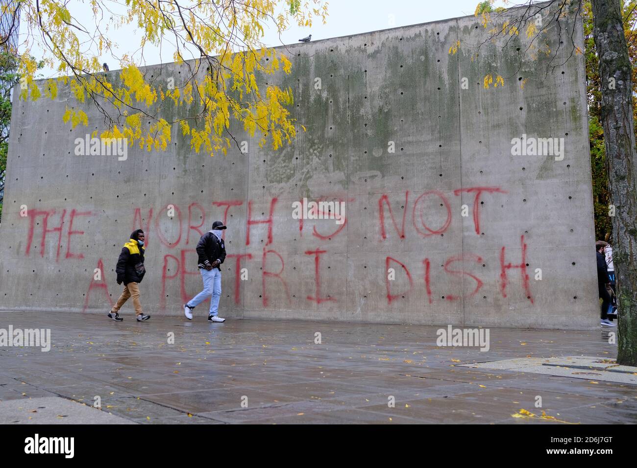 Manchester Piccadilly Gardens muro dipinto con blocchi di protesta graffiti IL NORD NON È UN PIATTO DI PETRI. Donna in maschera a piedi da esso. Foto Stock
