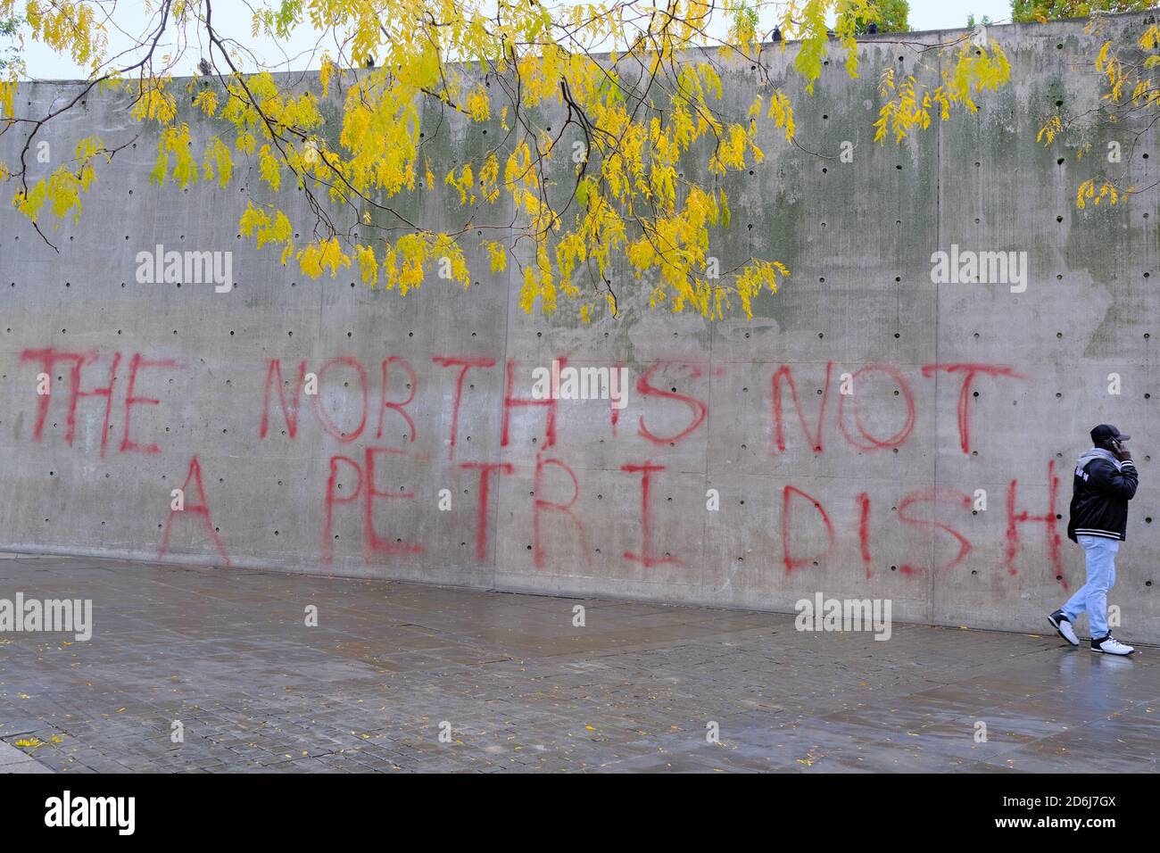Manchester Piccadilly Gardens muro dipinto con blocchi di protesta graffiti IL NORD NON È UN PIATTO DI PETRI. L'uomo cammina da esso. Foto Stock