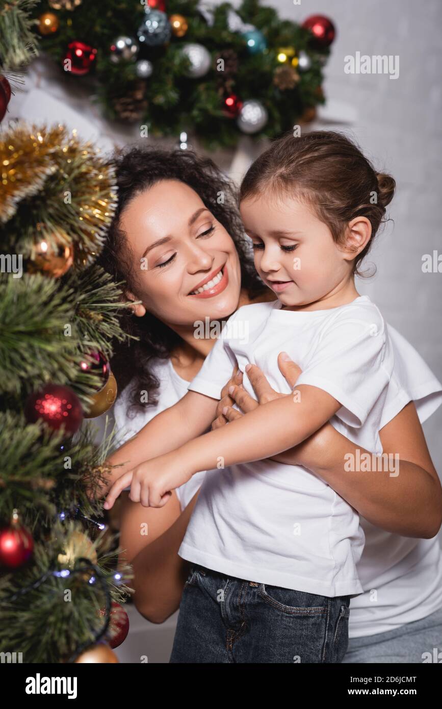 Madre abbracciando figlia vicino pino festivo a casa Foto Stock