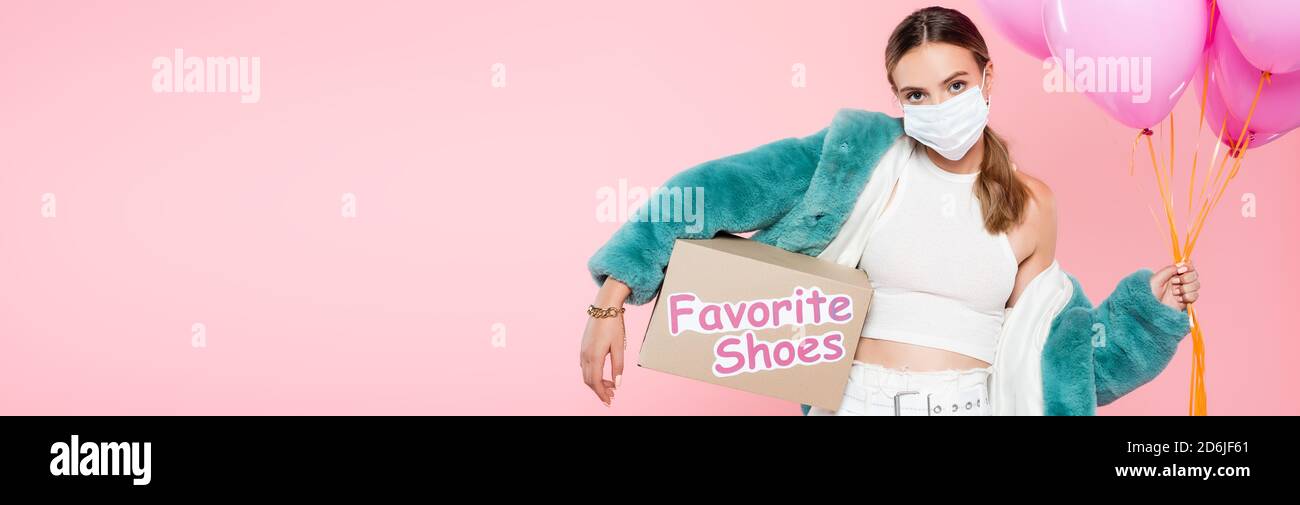 colpo panoramico di giovane donna in scatola di tenuta maschera medica con i caratteri delle scarpe e i palloncini preferiti in rosa Foto Stock