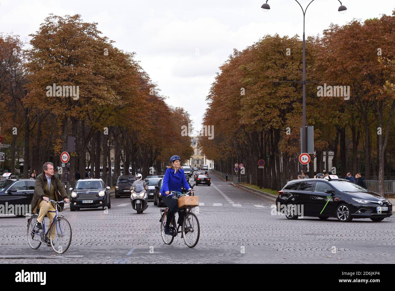 Parigi, Francia: Una coppia in bicicletta con altro traffico sulla strada lungo gli Champs Elysees in una giornata nuvolosa Foto Stock