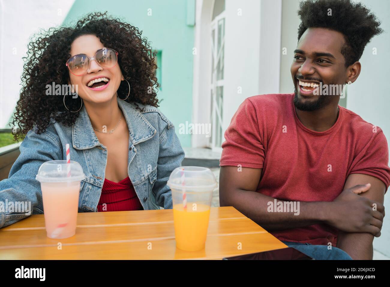 Ritratto di due amici afro che si divertono insieme e si godono del tempo mentre si beve succo di frutta fresca all'aperto presso la caffetteria. Foto Stock