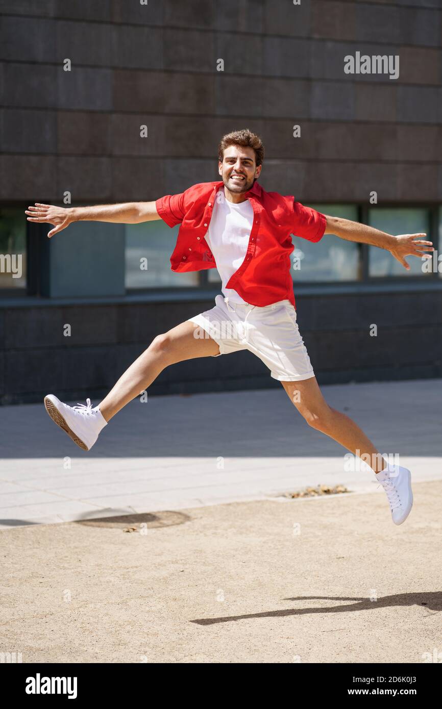 Uomo che indossa abiti casual che saltano su sfondo urbano. Foto Stock