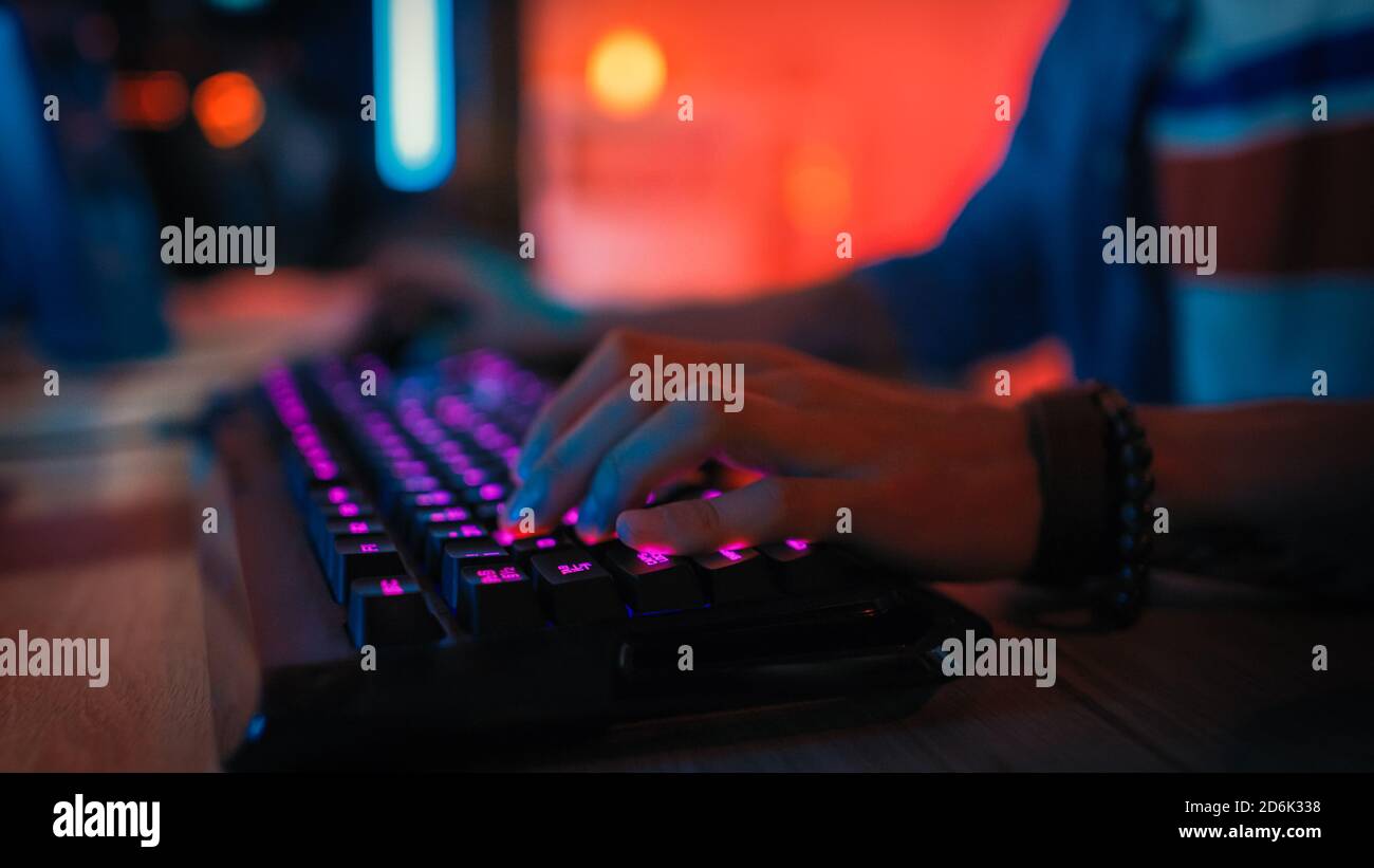 Primo piano Hands Shot che mostra un giocatore che preme i pulsanti della tastiera durante la riproduzione di un videogioco online. LED della tastiera. Il giocatore indossa un braccialetto Foto Stock